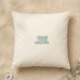 A square cream organic cotton cushion rests on fine golden sand. In the center, bold dusty blue lettering with a thin green outline reads “Chase your dreams.” A small white quartz crystal sits in the bottom left corner, and a sprig of silver green eucalyptus reaches in from the bottom right.